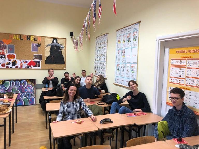 Nauczycielka i uczniowie siedzą w ławkach w pracowni języka angielskiego.