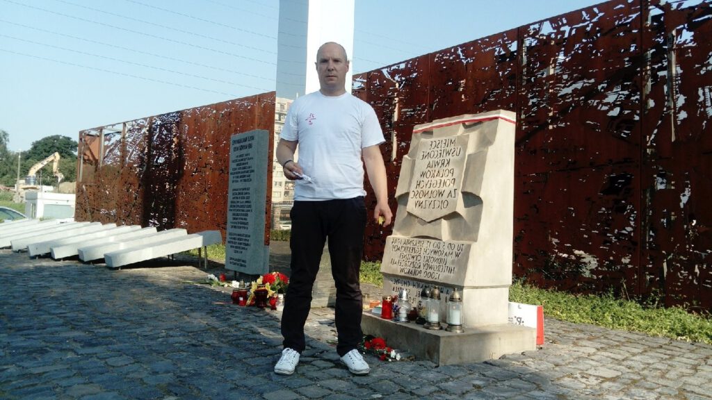 Słuchacz stoi przy postumencie upamietniającym miejsce rozstrzelania Polaków w czasie II wojny światowej
