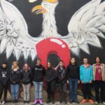 Kilkoro uczniów stoi na tle muralu z białym orłem
