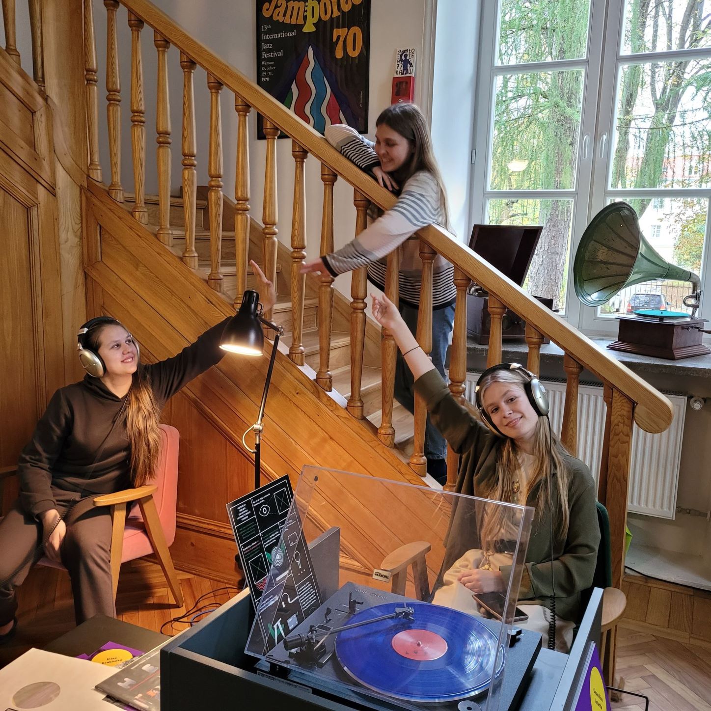 Trzy słuchaczki siedzą w czytelni ze słuchawkami na uszach przed gramofonem z płytą