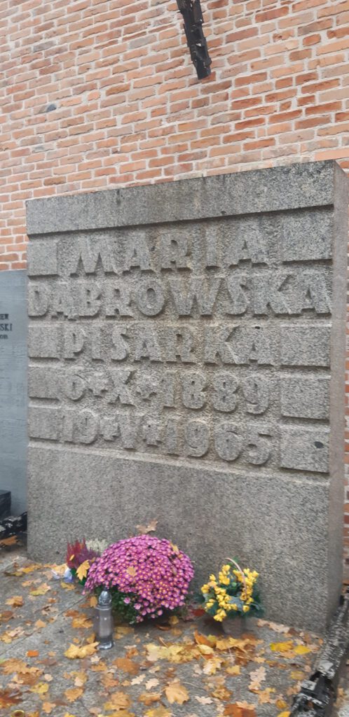 Granitowa płyta nagrobkowa z napisem Maria Dąbrowska pisarka. W tle mur z cegły.