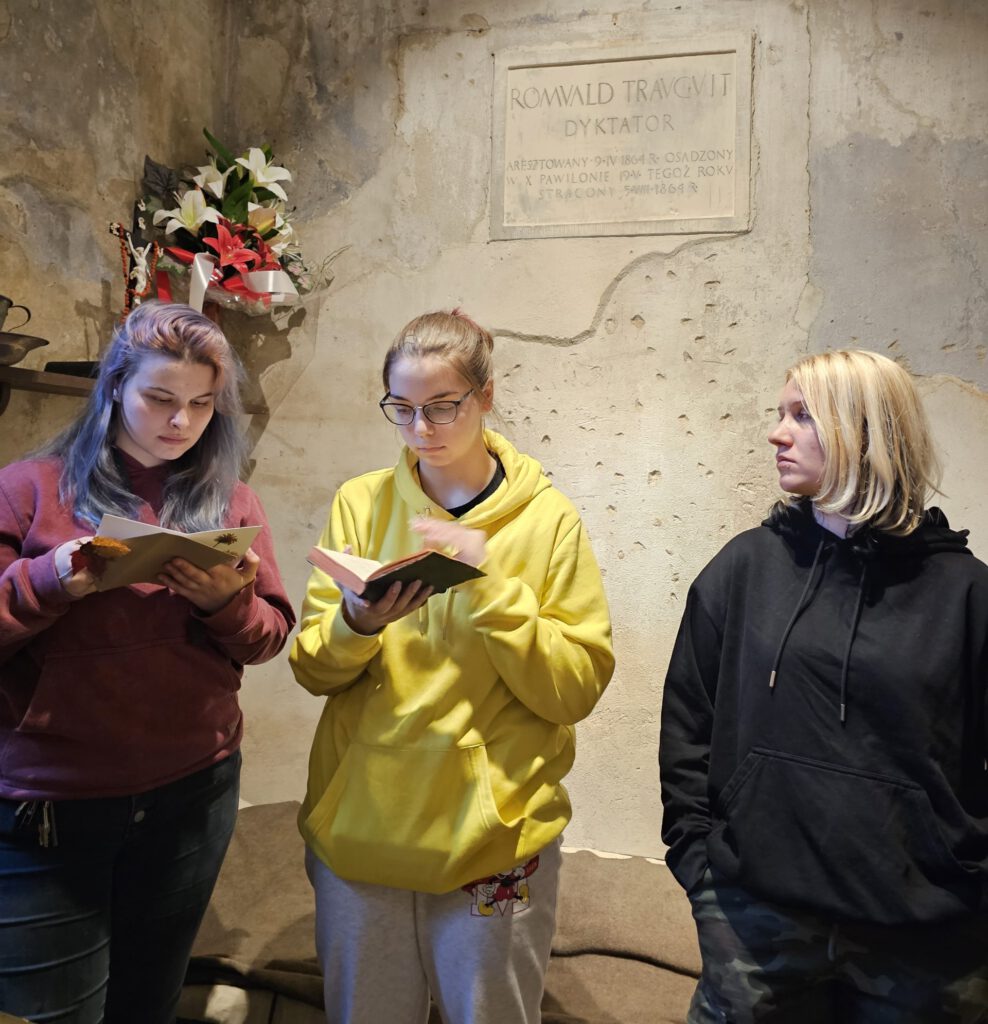Trzy uczennice stoją pod ścianą i trzymają w rękach otwarte książki