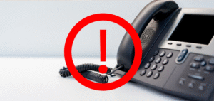 Zdjęcie przedstawiające czarny telefon stacjonarny. Po środku widnieje czerwony wykrzyknik w kółku, sugerujący problem.